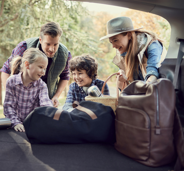 Family preparing for trip by loading trunk of car with luggage